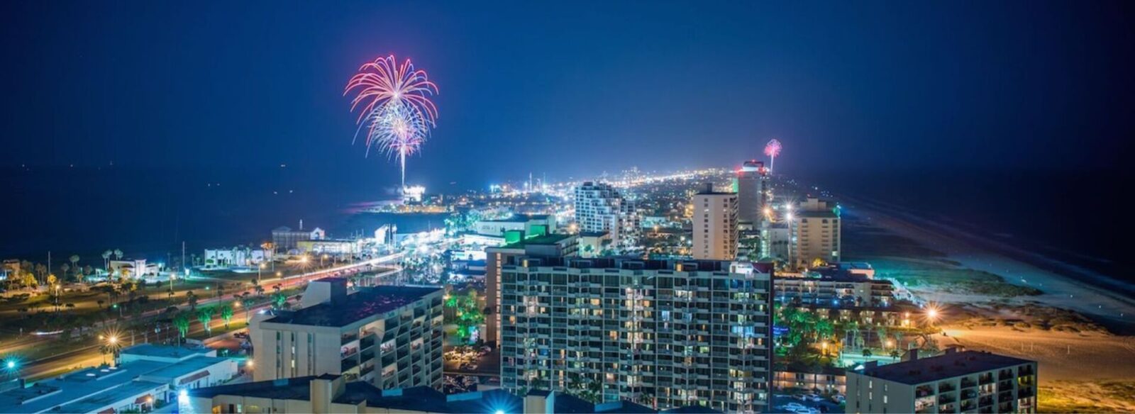South-Padre-Island-skyline-fireworks-displays | South Padre Island Vacation Rentals A vibrant display of colorful fireworks illuminating the night sky above illuminated high-rise condo buildings and hotels.