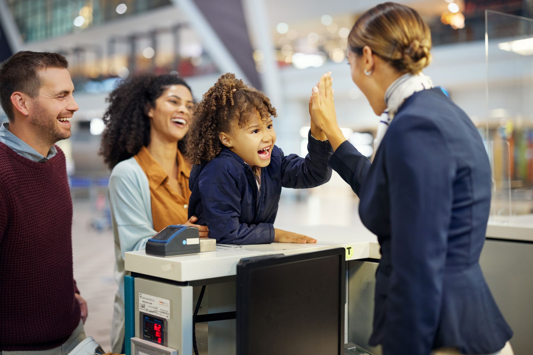 Two smiling hospitality professionals helping a child at a front desk counter, representing top-tier customer service.
