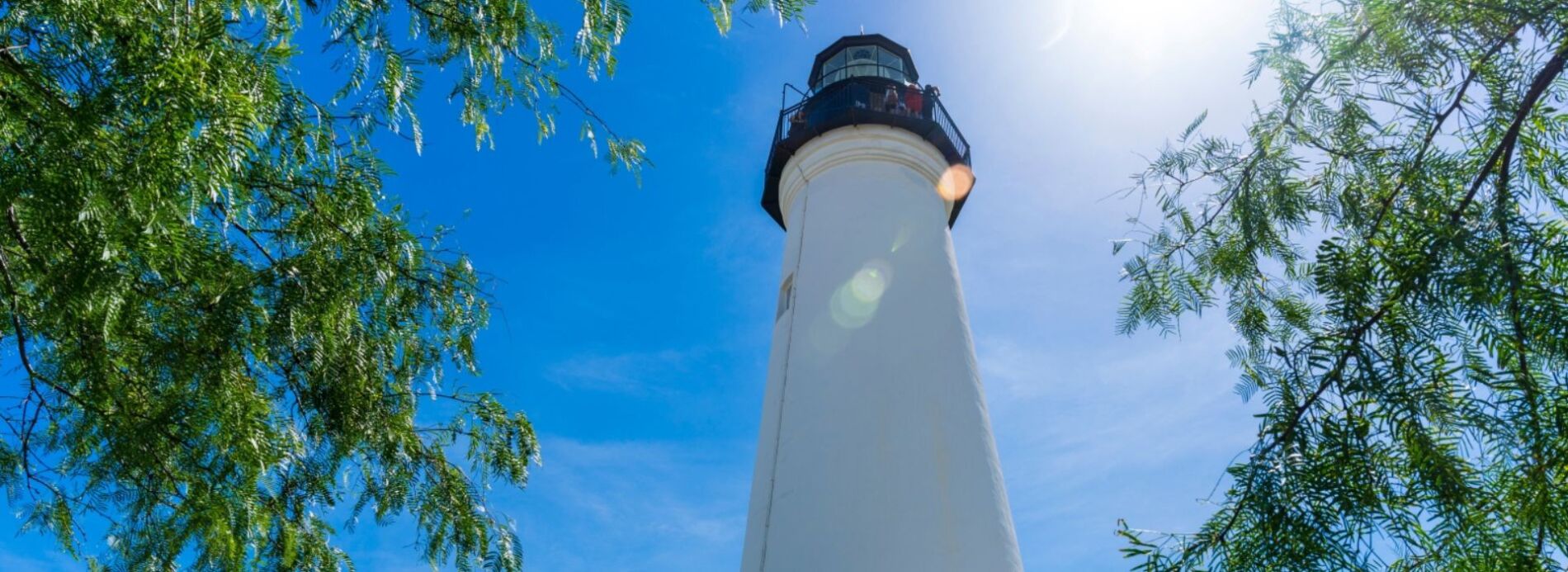 A striking low-angle shot looking straight up at the historic white stone Port Isabel Lighthouse against a crisp blue sky.
