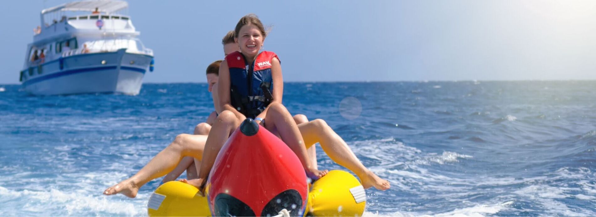Children wearing life jackets riding an inflatable yellow banana boat towed across rolling ocean waves, highlighting exciting watersports.
