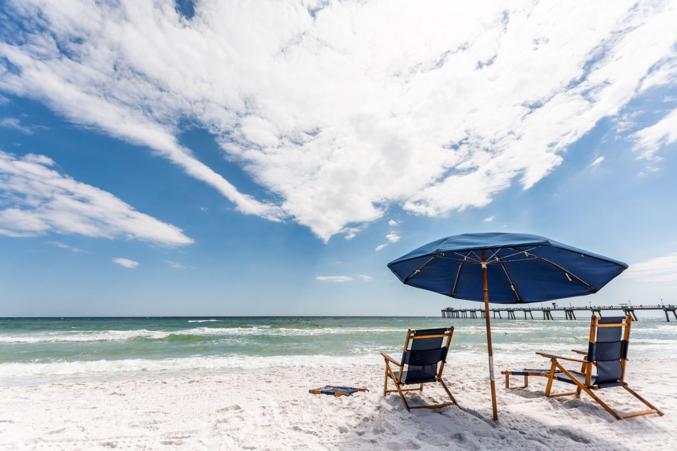 Relaxing-under-beach-umbrellas-on-the-Gulf | South Padre Island Vacation Rentals Beach lounge chairs and a royal blue umbrella set up on the soft sand under a dynamic blue sky with clouds.