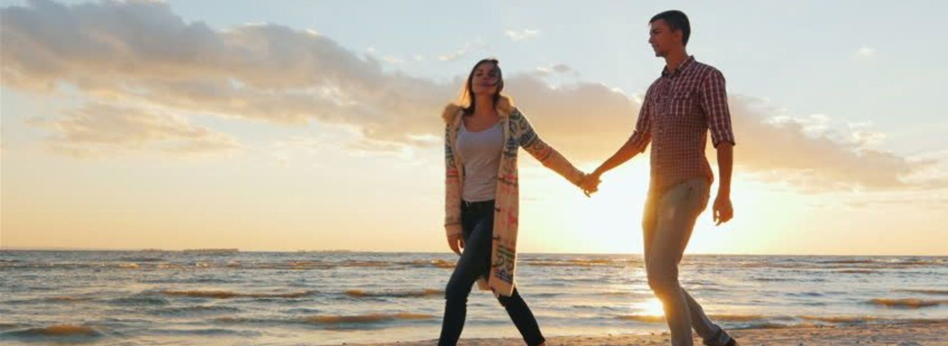 A happy couple holding hands and smiling while strolling along the shoreline during a warm golden hour sunset on South Padre Island.
