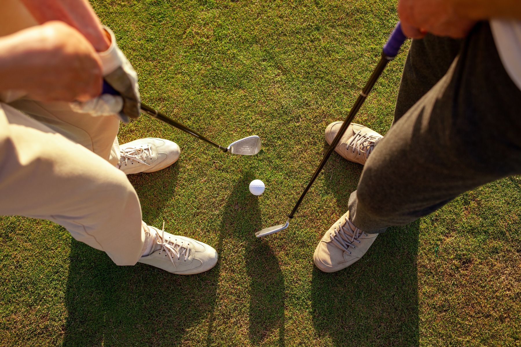 Low-angle perspective of golfers aligning a putt on a pristine green golf course on a sunny day.