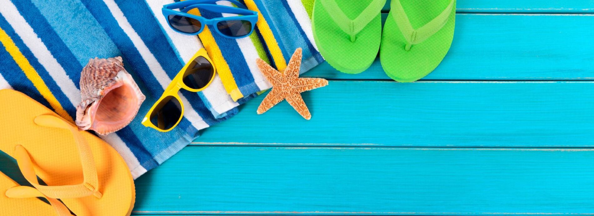 A bright green pair of flip-flops, a striped beach towel, and a natural dried starfish arranged on a vibrant blue wooden surface.