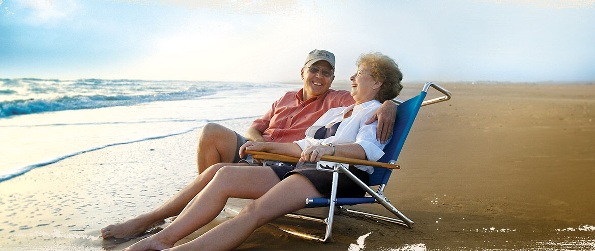 Relaxing-in-the-sand-during-golden-hour | South Padre Island Vacation Rentals A mature couple sitting together in beach lounge chairs, enjoying the relaxing ocean breeze at sunset.