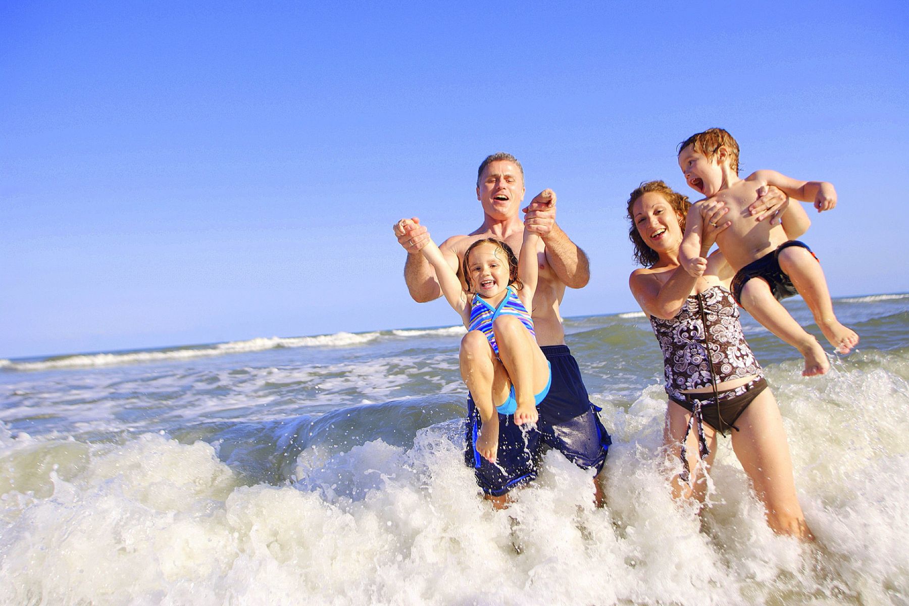 A joyful father lifting his children up while playing in the shallow ocean waves during a South Padre Island vacation.