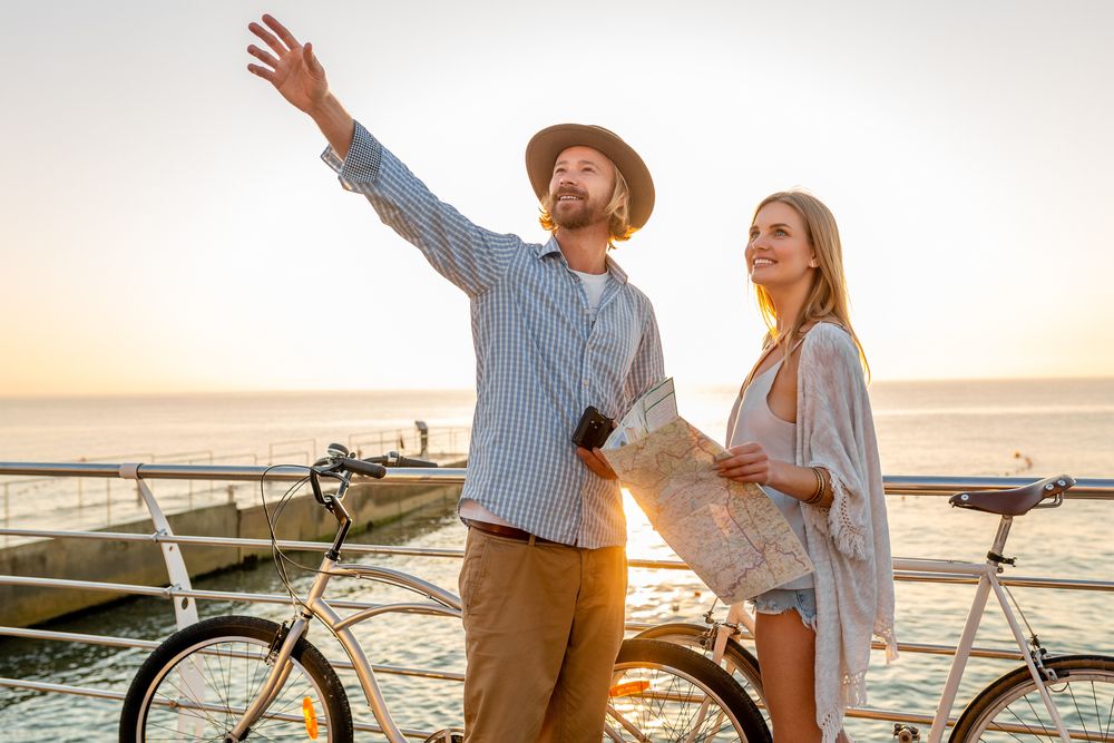 A happy couple standing on the shore next to their bicycles on a bright morning, highlighting romantic coastal escapes with Padre Getaways.